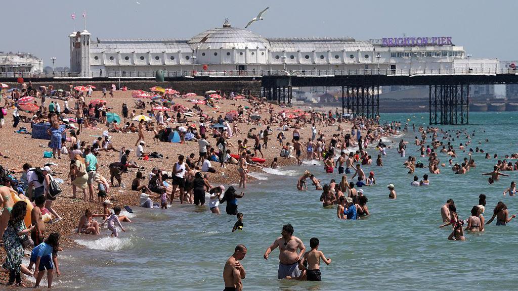 People on the beach and in the sea at Brighton. Brighton Pier is in the background.