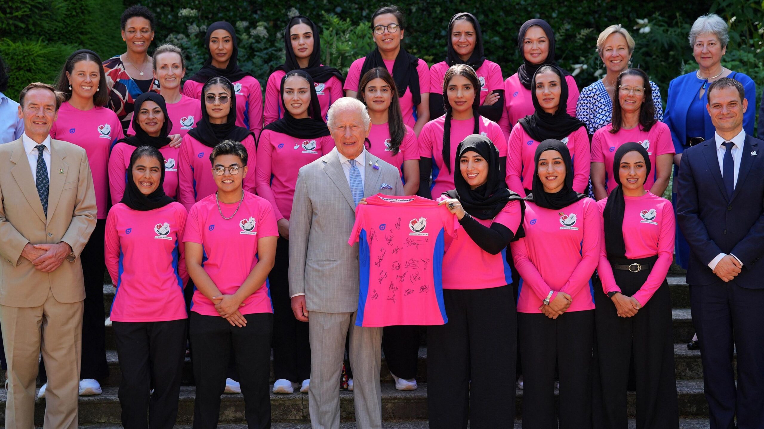 Members of the Afghanistan women's cricket team pose with King Charles, who is holding a signed shirt