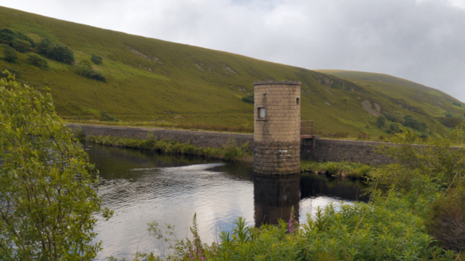 A view of the reservoir surrounded by green moors and a tower.