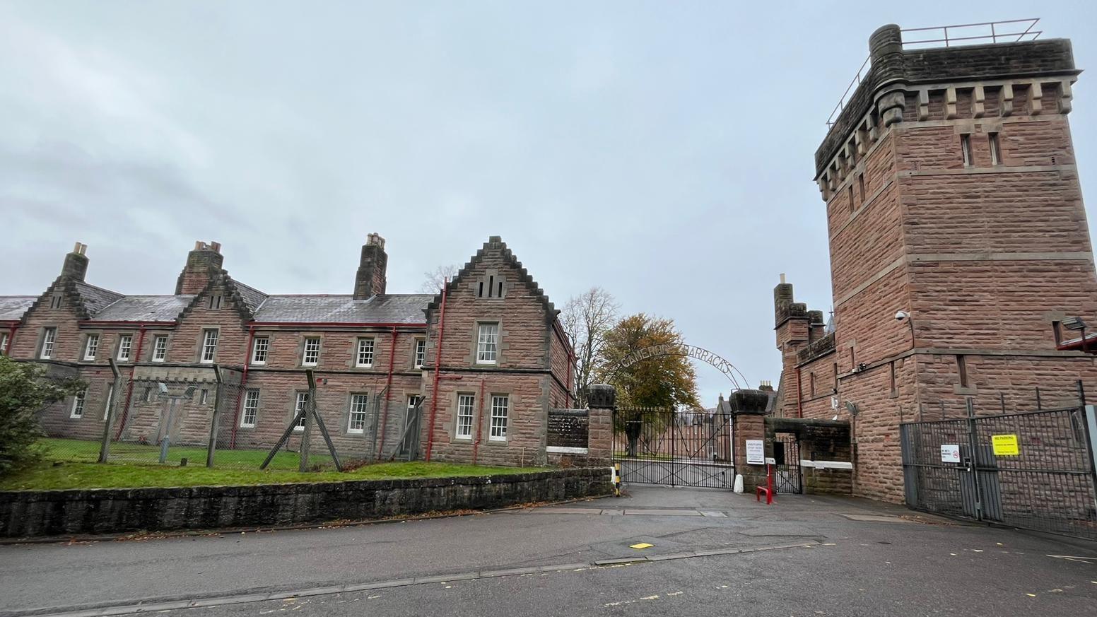 The barracks is a group of traditional, brick-built buildings with long narrow windows with white frames. The complex is surrounded by a high, wire fence.
