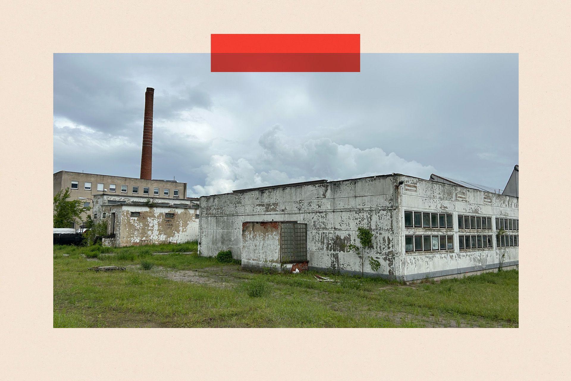 An abandoned concrete building with a cooling tower in the background