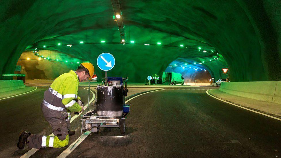 Tunnel in the Faroe Islands being maintained by a worker. A large underground roundabout with ceiling lights.
