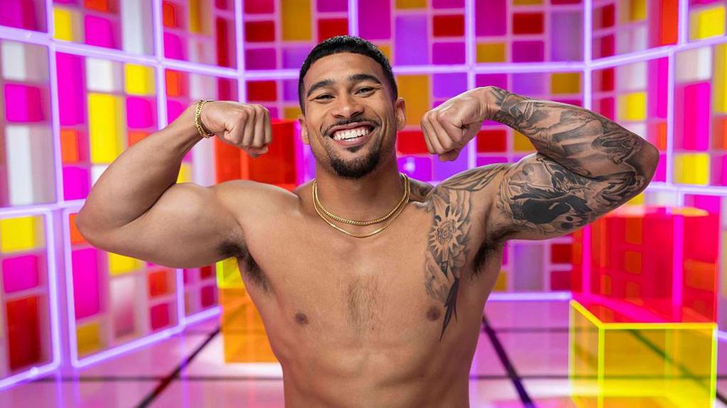 Sean Reifel seen posing shirtless while flexing his muscles in front of a colorful backdrop as part of a Love Island USA photoshoot.