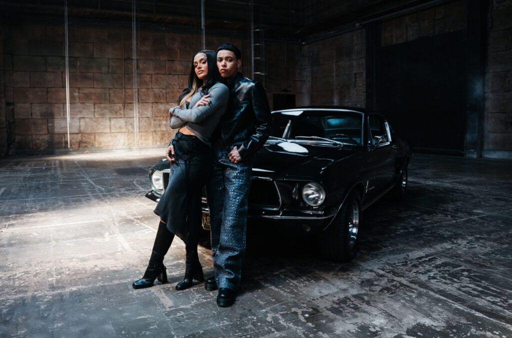 KWN and Kehlani lean against a black Ford Mustang, on the set of the video for Worst Behaviour.