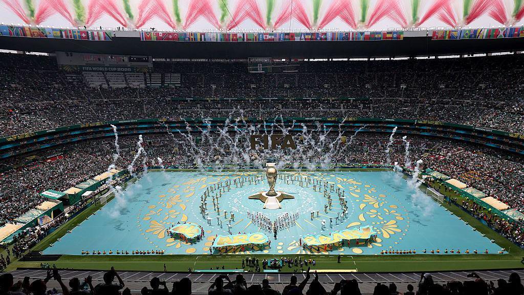 A wide view of the Azteca Stadium with a World Cup trophy in the middle of the pitch
