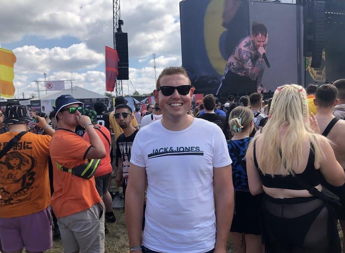 A man in a white T-shirt smiles in a festival crowd.