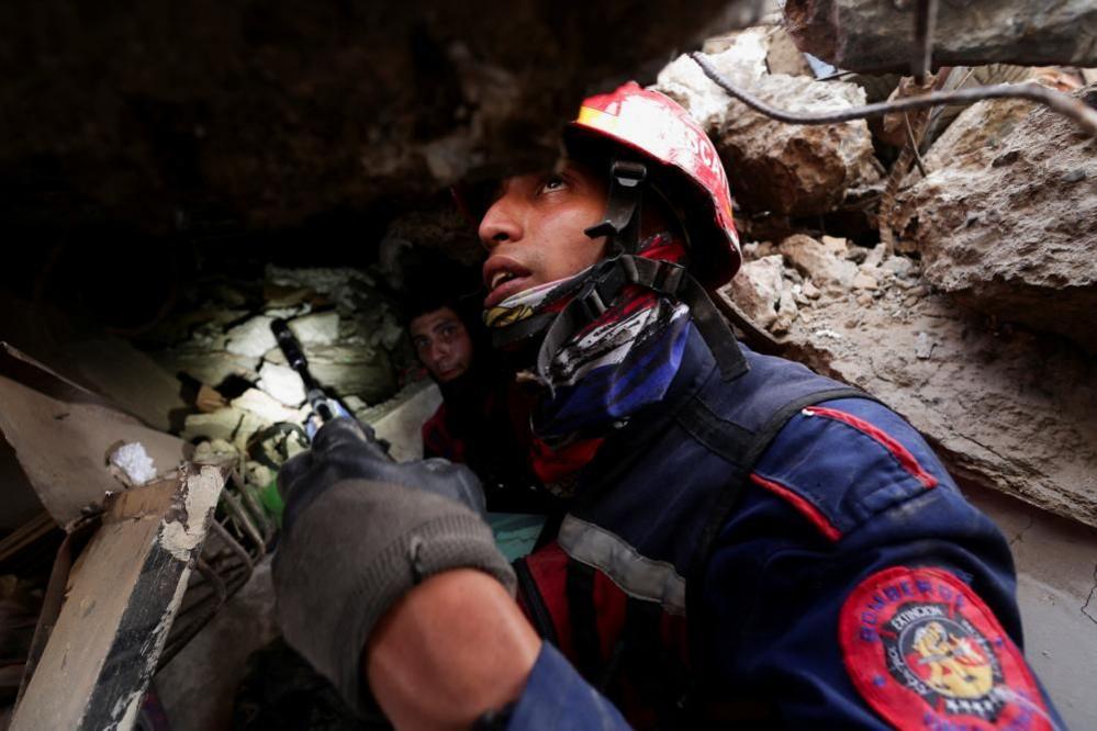 A firefighter, wearing a helmet and heavy duty coat, holds a small search camera in his hand as he searches for earthquake survivors.