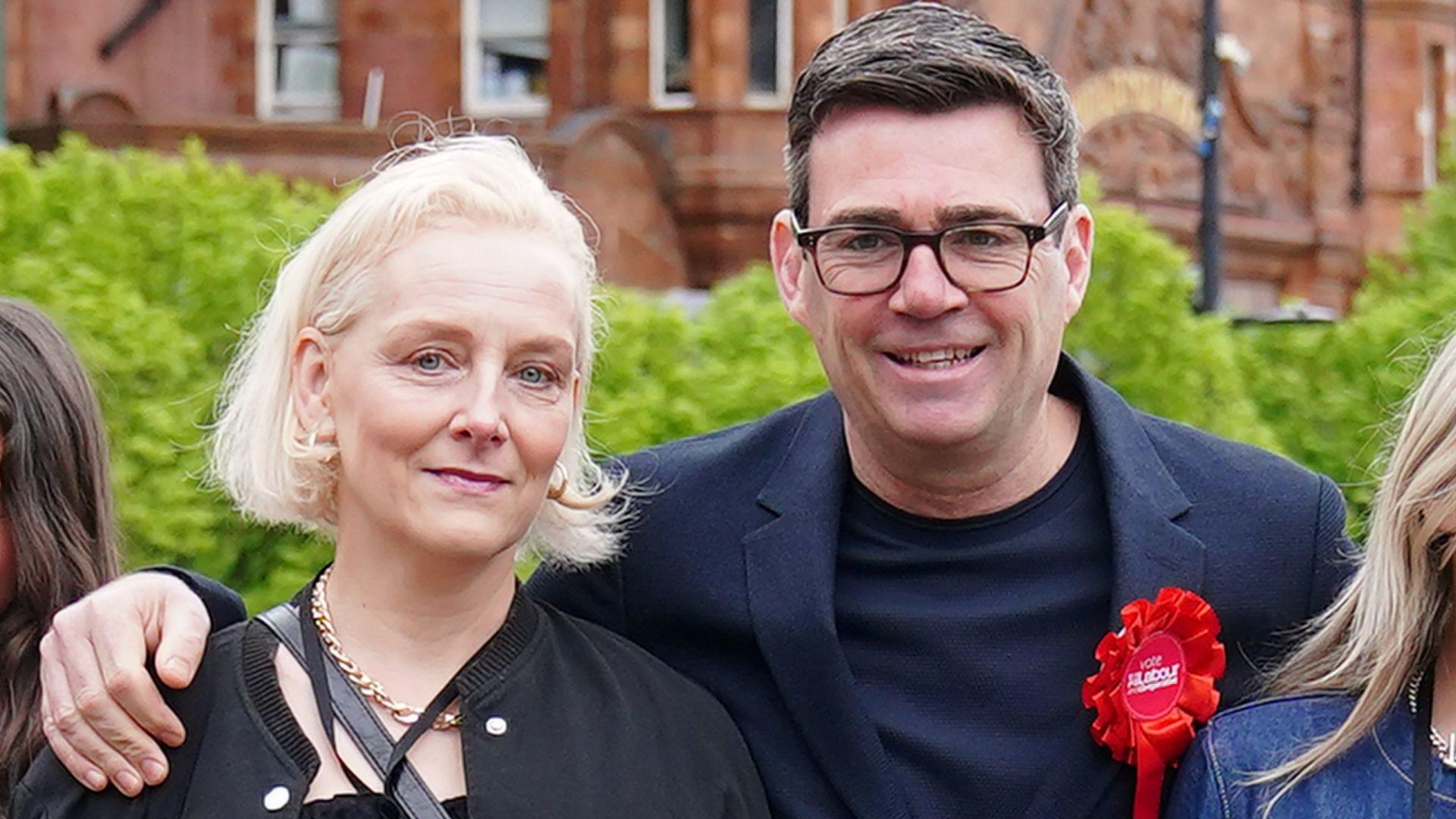 Andy Burnham, wearing glasses and a blue jacket and T-shirt with a red Labour rosette, and Marie-France Van Heel, with blonde hair and wearing a black top, smile at the camera