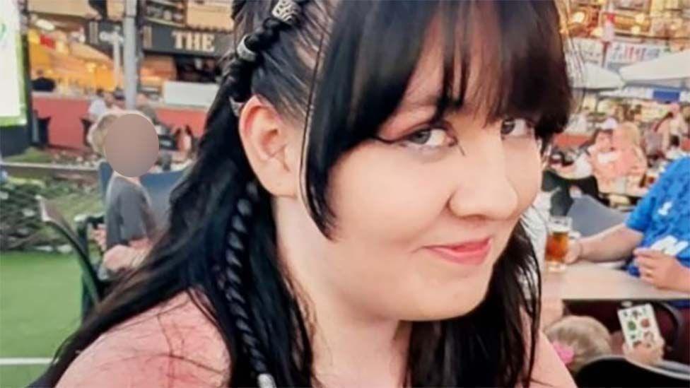 A girl with dark hair and a pink top smiles at the camera.