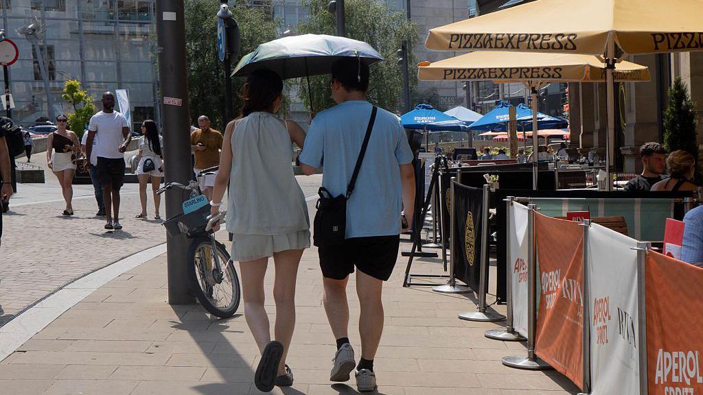 two people walking in the street holding umbrellas to shield them from the hot weather