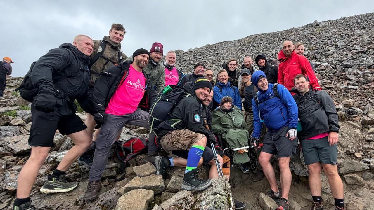 A group of people stand on a mountain, including a boy in a wheelchair with Catherine, the Princess of Wales, stood next to him.