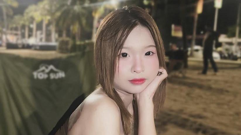 A young girl with dark straight hair and eyes looks at the camera with her head propped up by one hand at night time.