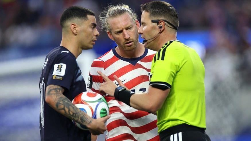 Referee Danny Makkelie speaks to the Miguel Almiron of Paraguay and USA defender Tim Ream during a VAR check for 'mistaken identify'