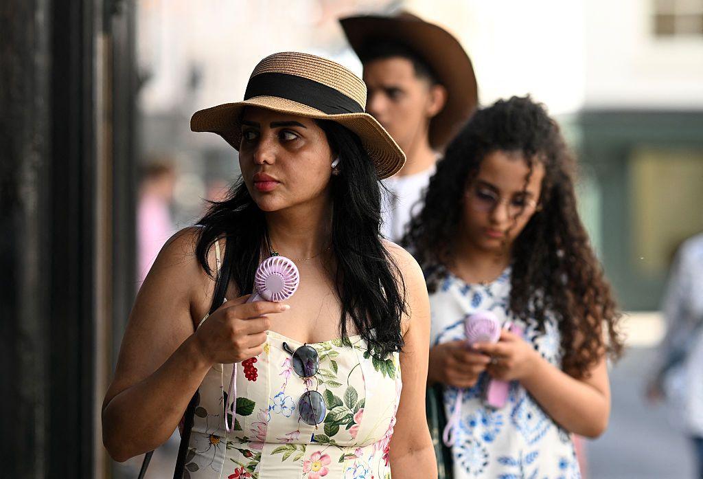 People use hand-held fans to cool themselves as they walk past shops in York, on June 24, 2026.