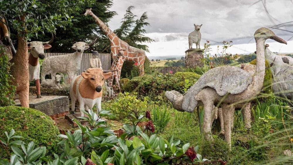 A selection of sculptures of animals in a country scene - they include cows, sheep and a giraffe