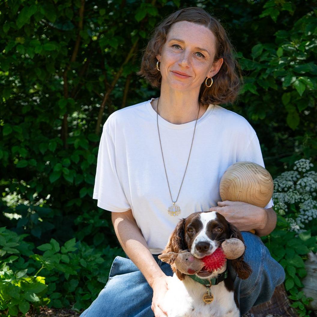 Kim Errington, with a small dog, holds a wooden ball