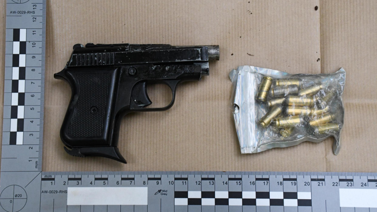 The converted starter pistol and home made bullets inside brown paper packaging. A square-angled ruler is around it to denote its size