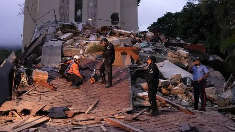 Rescue workers and police stand on the roof of a collapsed building amid rubble after an earthquake.