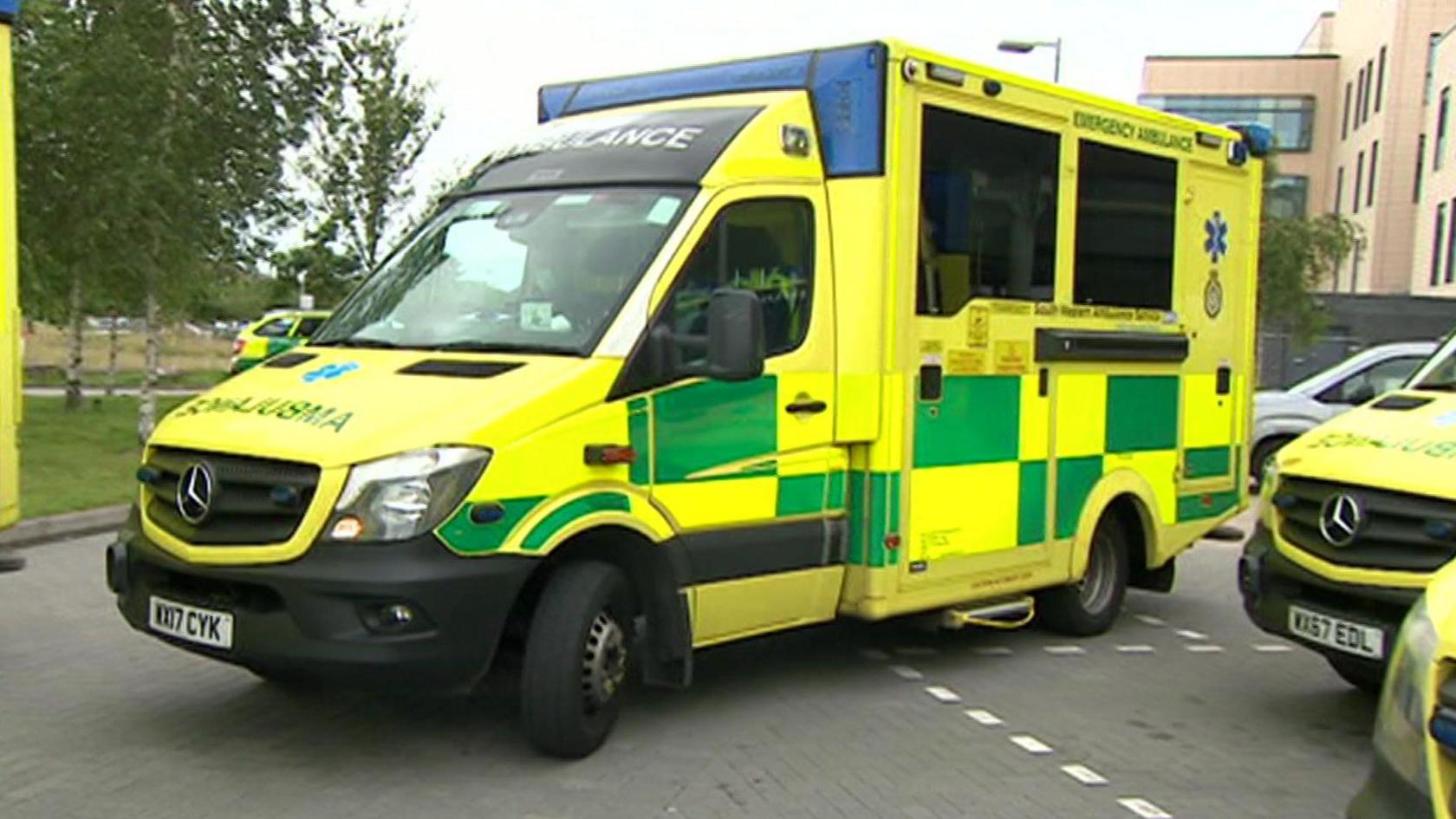 An ambulance pulls out of a parking space. It is yellow and green.