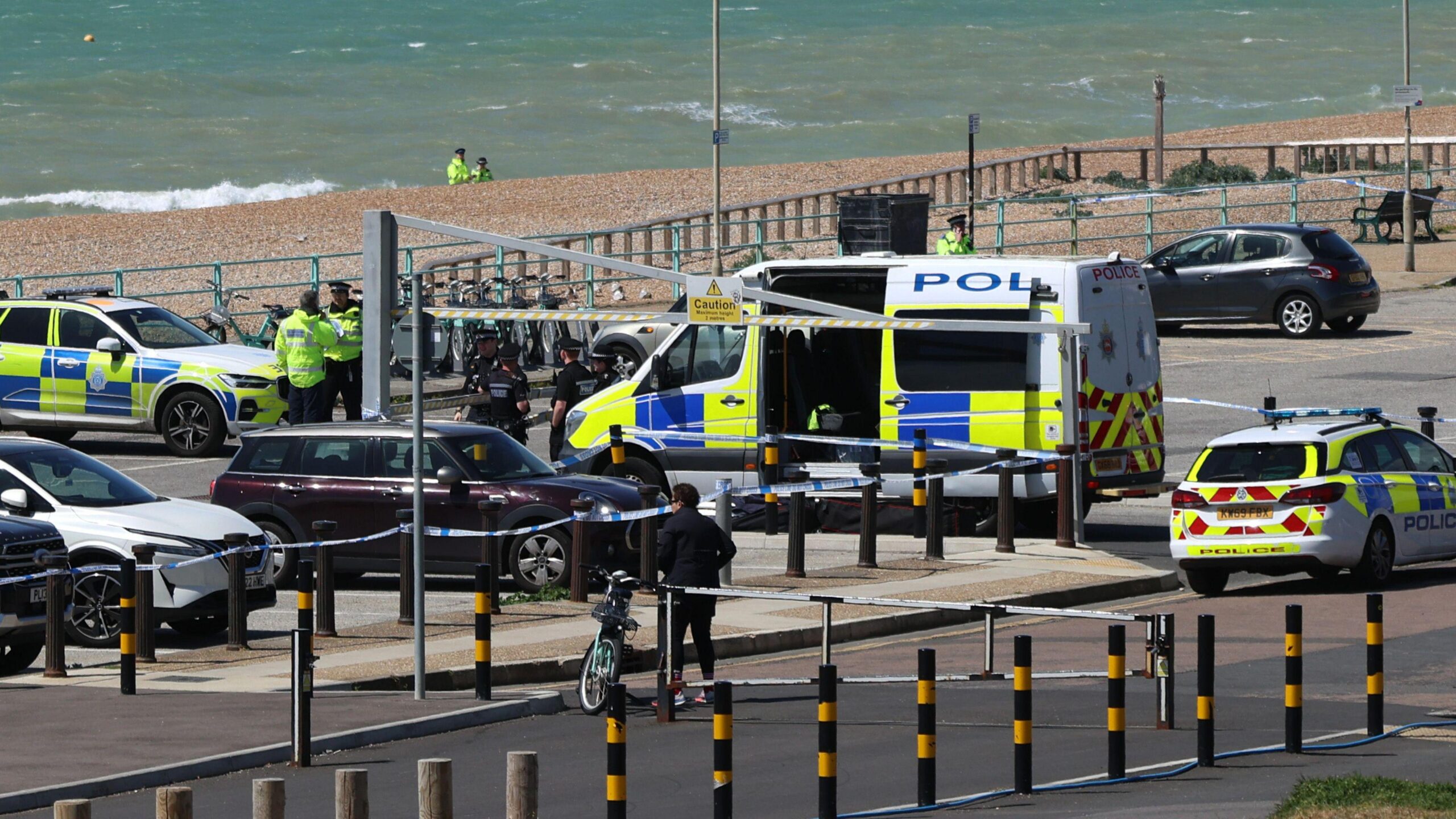 Police vehicles and officers in the Black Rock car park on Madeira Drive after the bodies of three women were recovered from the sea in Brighton. The car park is next to a pebble beach, where two more officers are standing in the distance