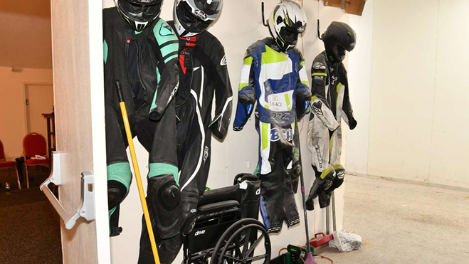 Four sets of motorcycle racing leathers and crash helmets hang from a wall at a funeral parlour.