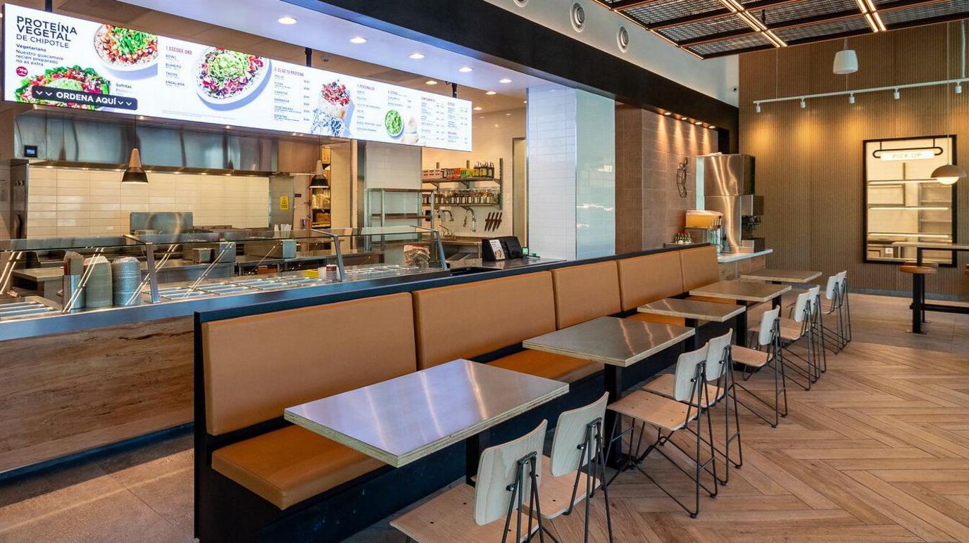 The interior of Chipotle's Nuevo León outlet, including a salad bar, ordering till and tables and chairs.