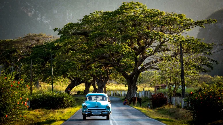 Classic American car rolls down a quiet rural country road in Valle de Vinales Cuba