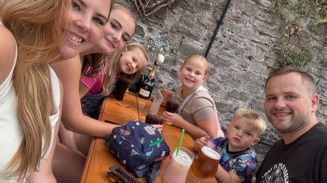 Claire with her four children and husband sit at a pub bench having drinks.