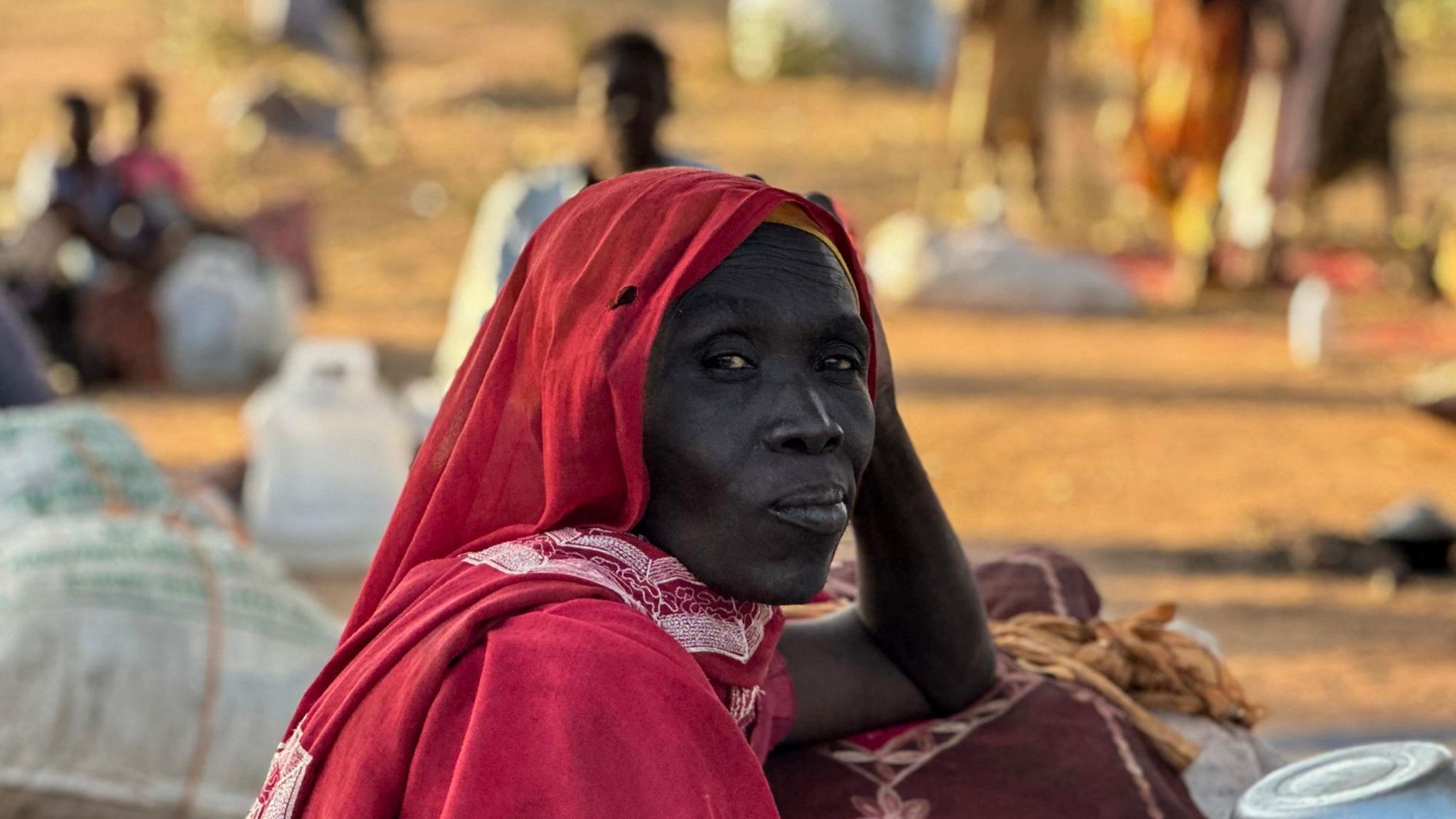 A woman wearing a red outfit and headscarf gazes past the camera