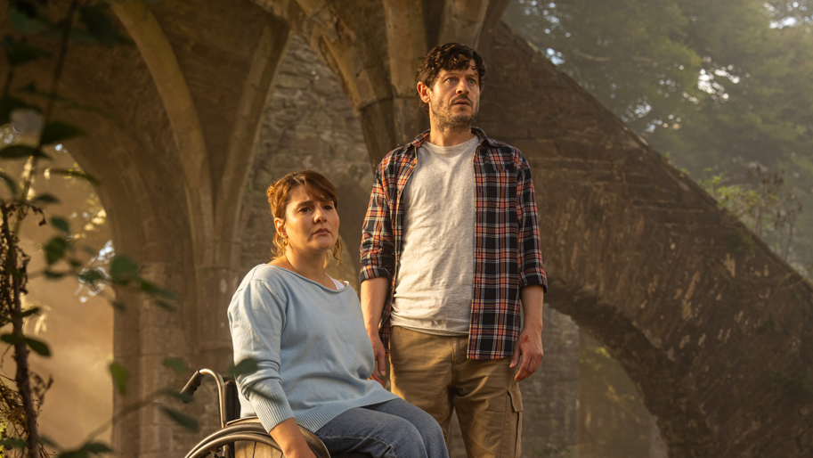 Ruth Madeley and Iwan Rheon in the new TV drama series. They both look concerned and are inside the ruins of an old building with trees behind.