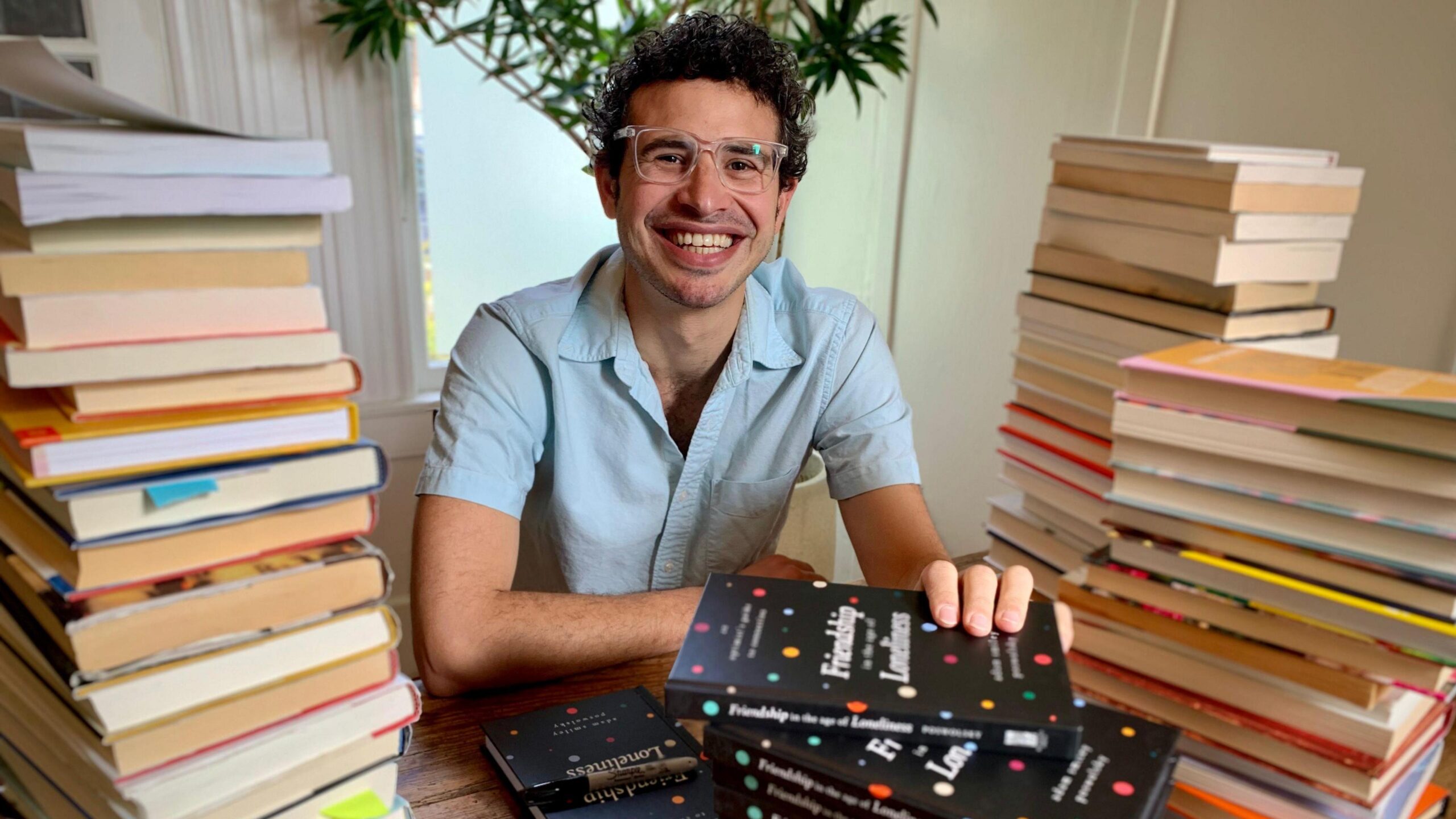 Adam Smiley Poswolsky sits in front of piles of books