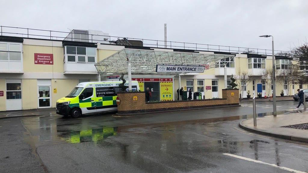 Frimley Park Hospital. A sign over a door says 'MAIN ENTRANCE.' An ambulance can also be seen.