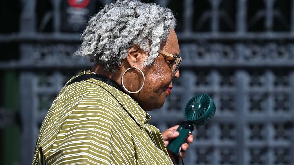 A woman uses an electronic fan to keep cool as temperatures soar in the United Kingdom