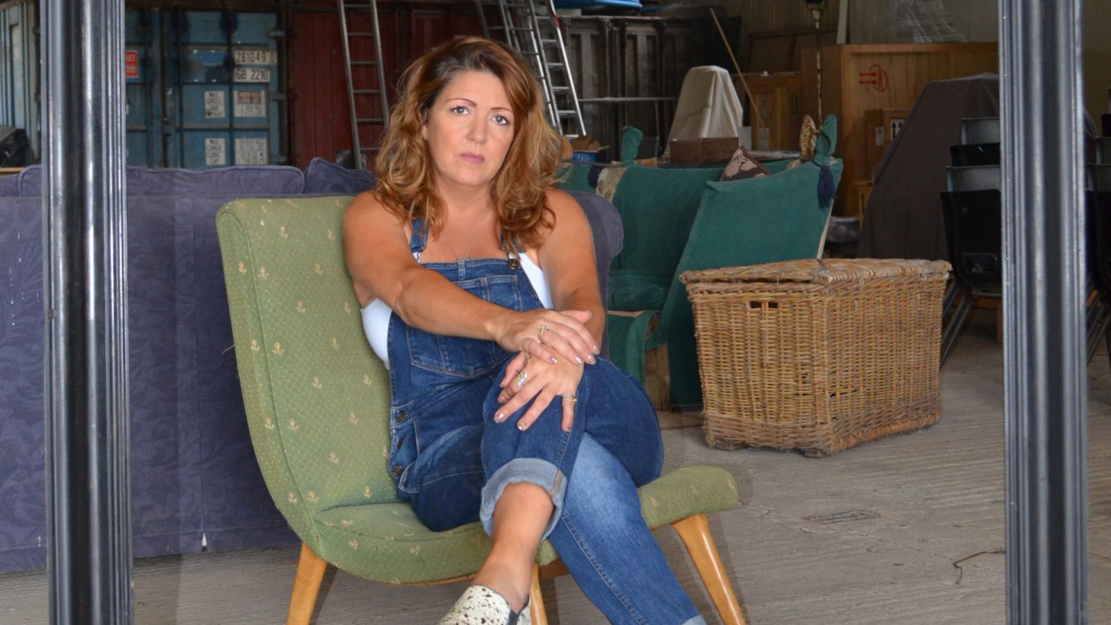 Lianne, sat on a big green chair in blue denim dungarees in a studio.