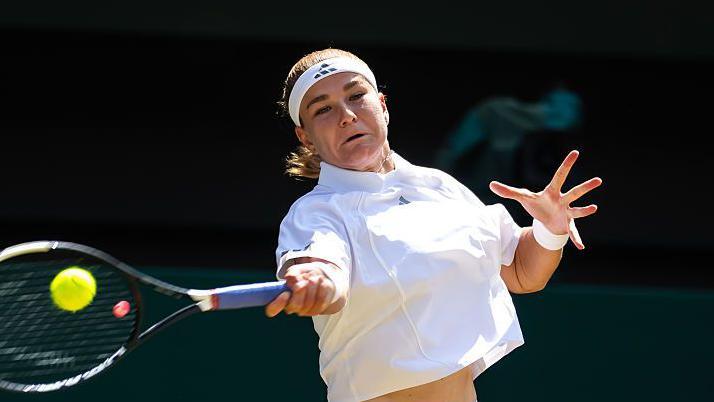 Karolina Muchova, wearing white tennis top and a white headband, hits a forehand as her face shows the strain of playing the shot