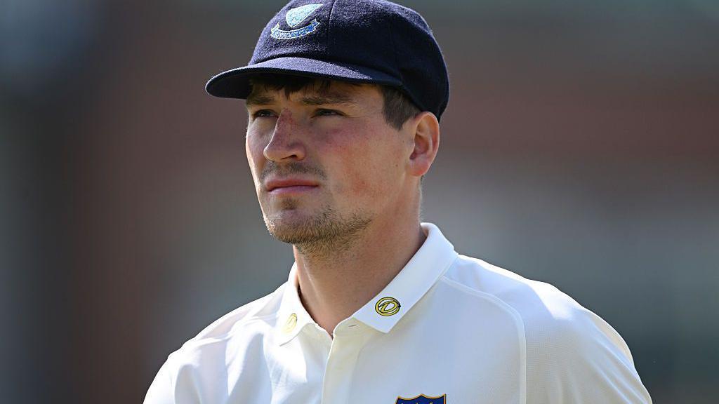 Henry Crocombe looks on in white Sussex shirt and dark blue Sussex cap