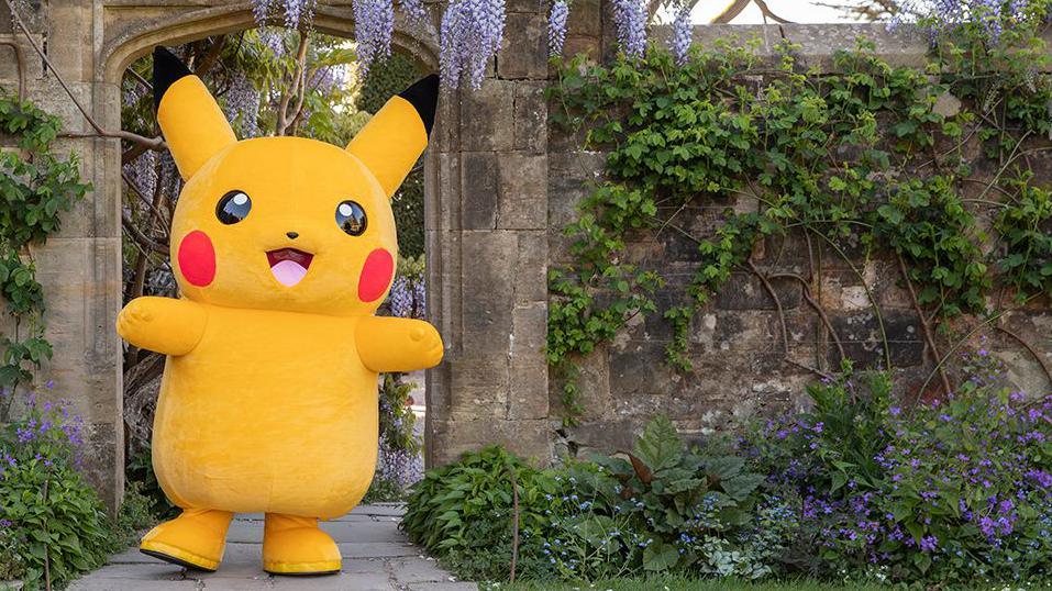 Pokemon character Pikachu standing in a stone doorway in a garden with an abundance of flowers owned by the National Trust on a sunny day.