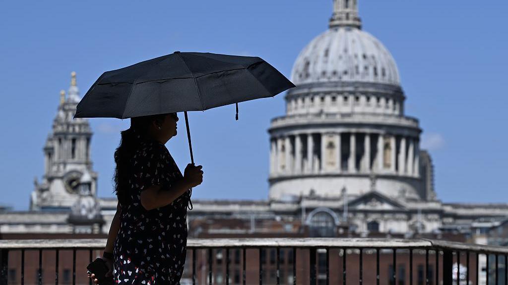 A woman walks under an umbrella past St Paul's Cathedral in London during the heatwave.