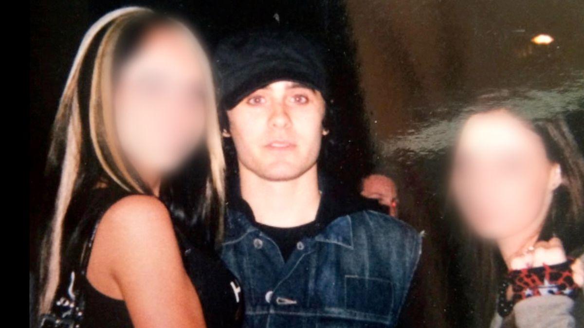 Jared Leto, wearing a denim jacket and a black hat, looks straight at the camera as he poses with two young girls whose faces we have blurred. On the left is a blonde girl, a little taller than Leto, and on the right is a shorter girl with dark hair. Their faces are brightly lit by the flash in a dark room.