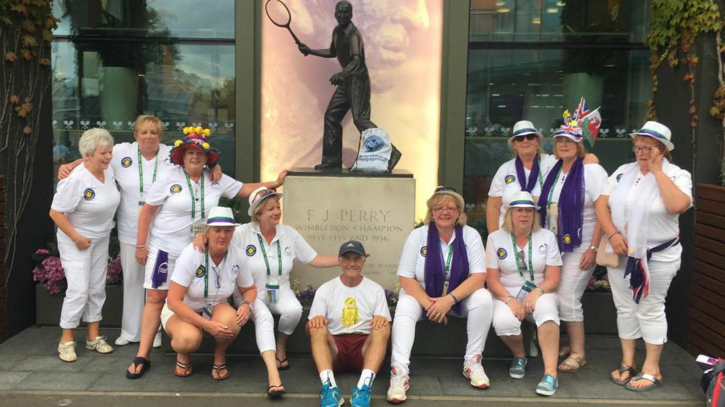 Geoff Hughes is sitting in the middle of a photo in front of a Fred Perry statue surrounded by members of the Andy Murray fan group The Murraynators