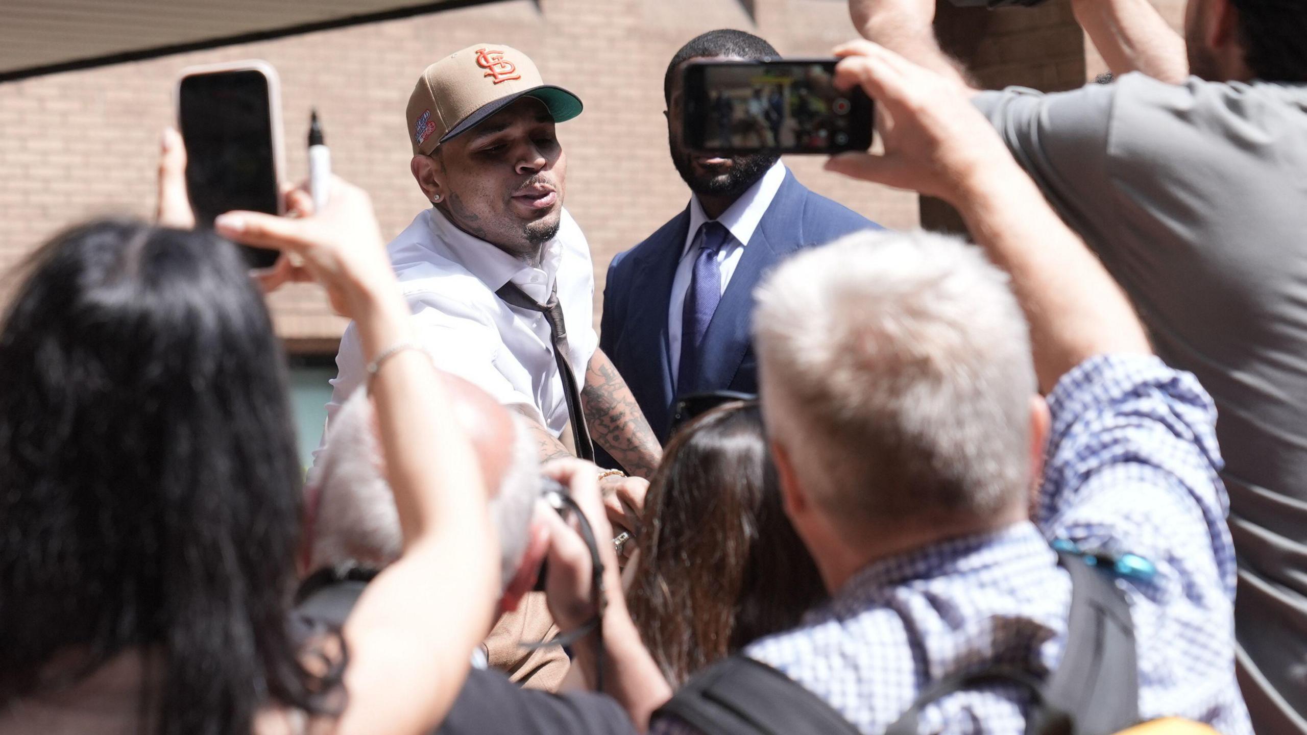 Chris Brown leaning into a small crowd outside court, with some holding up their phones