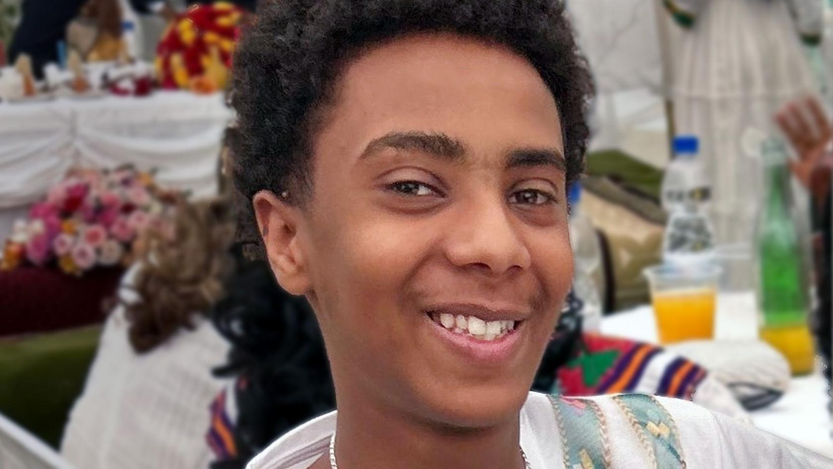 A young boy with short dark curly hair smiling at the camera.