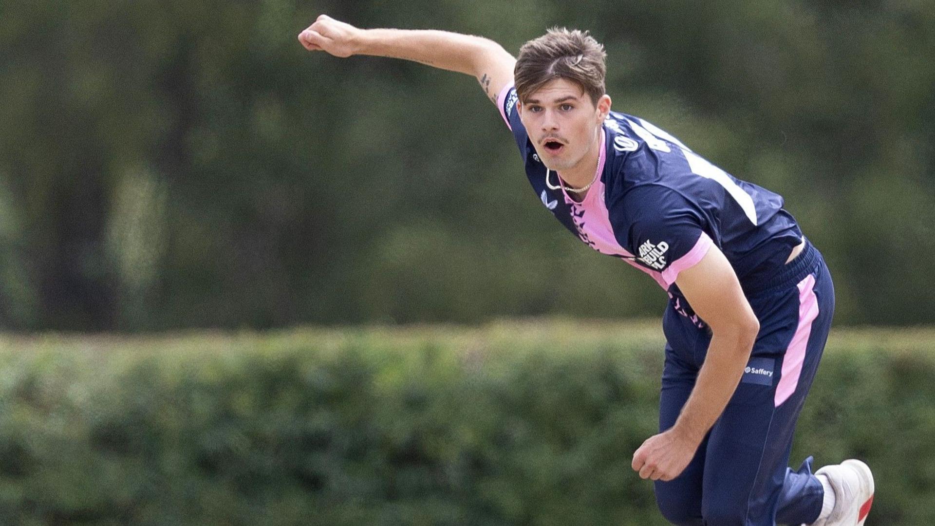 Noah Cornwell bowls left-arm seam in the blue and pink kit of Middlesex