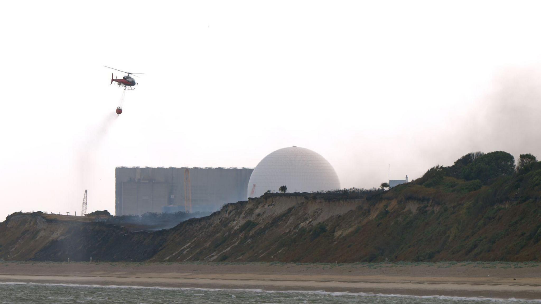 A helicopter flies water collected from the sea to drop on the wildfire at Dunwich Heath, near Leiston, close to the Sizewell B nuclear power station, where a major incident has been declared as firefighters battle a large heathland blaze on the Suffolk coast.