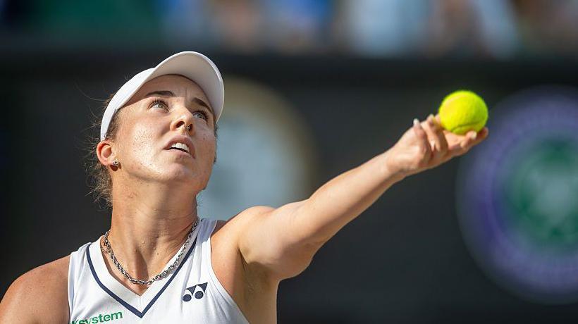 Linda Noskova prepares to serve, looking upwards and holding the tennis ball in her left hand