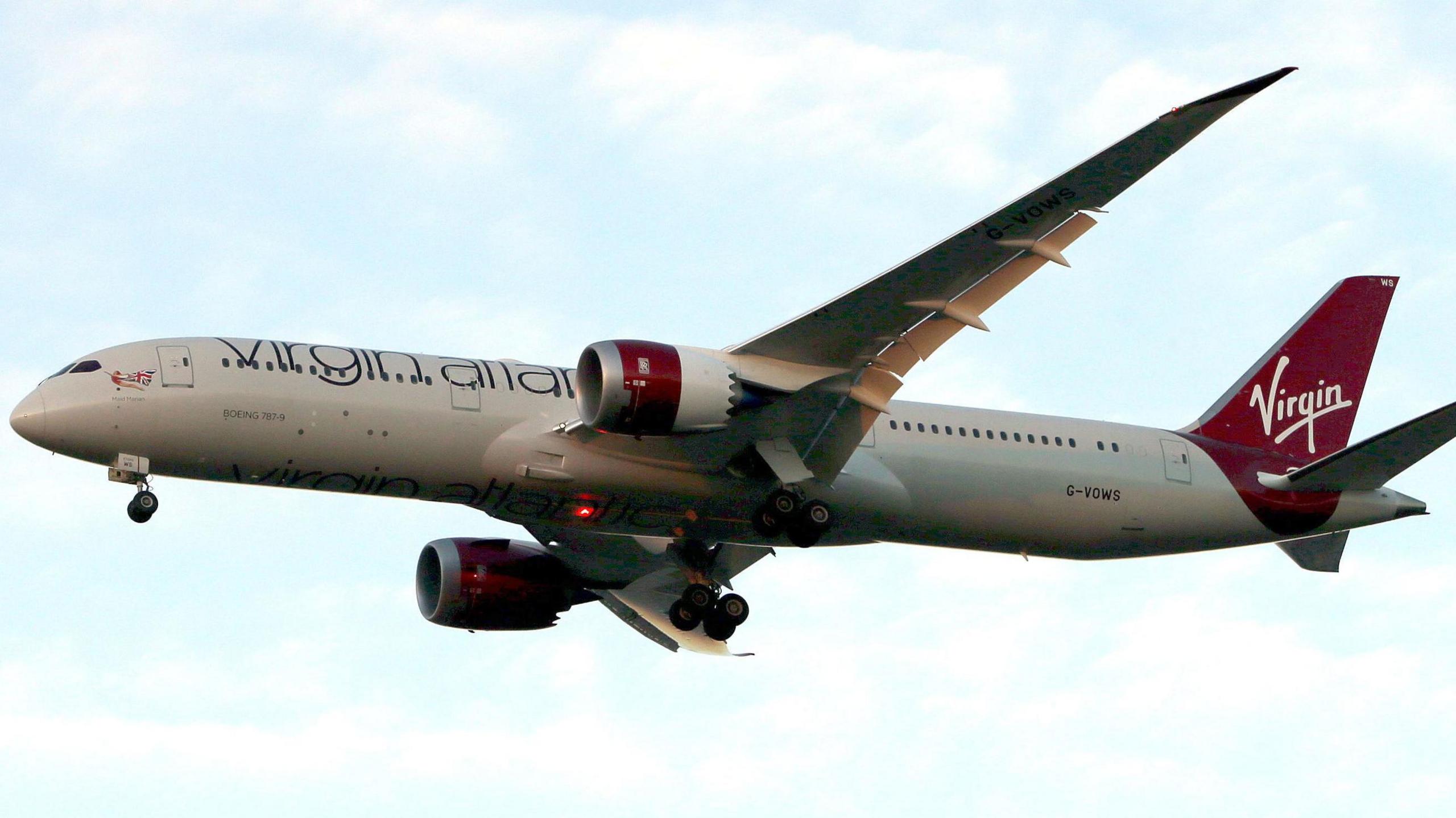 A large white passenger plane in flight. It carries red Virgin Atlantic branding.