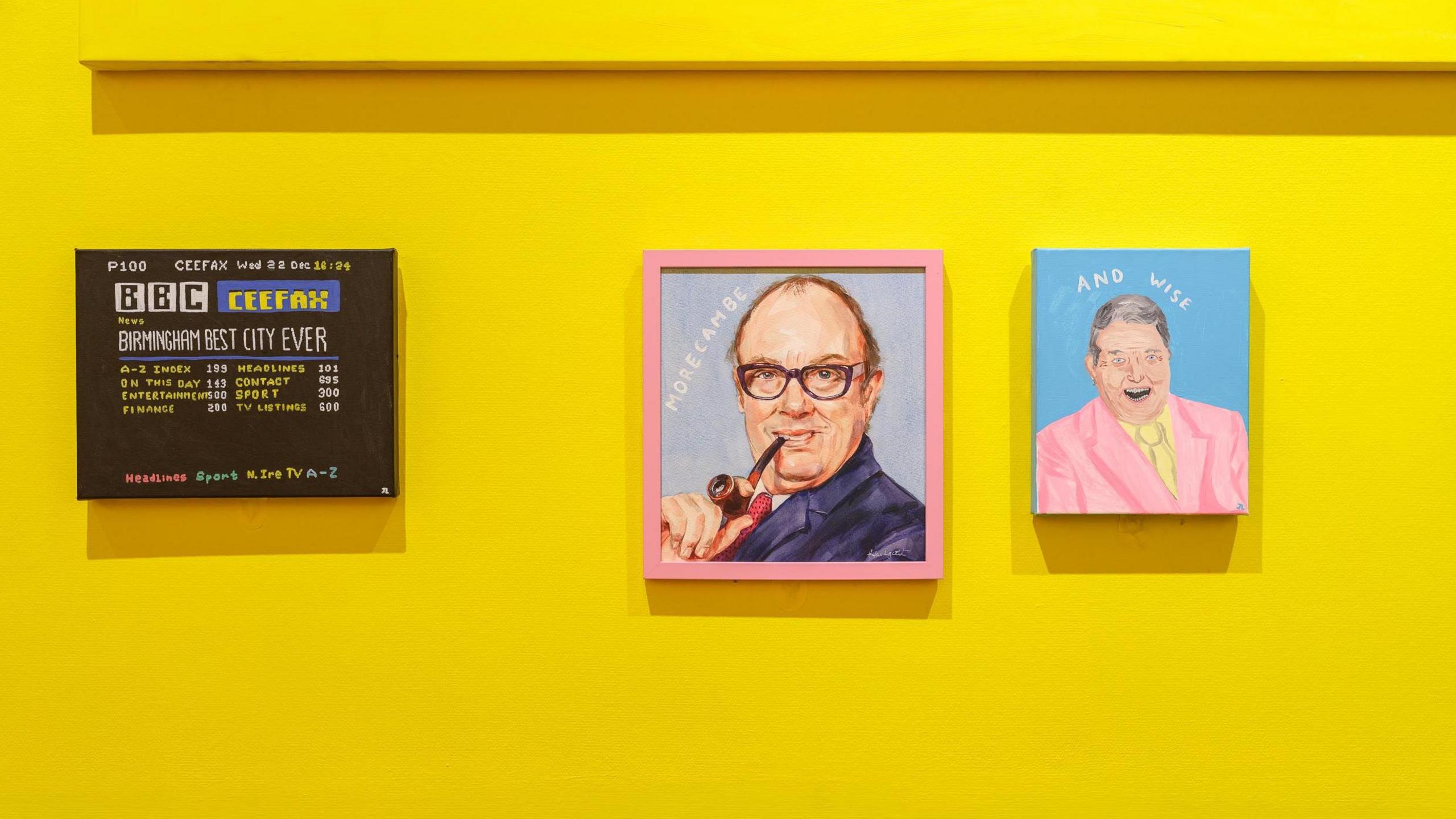 Canvas paintings hung on a yellow gallery walls depicting Ceefax and comedians Morecambe and Wise. Morecambe is holding a pipe to his mouth and Wise smiling broadly in a pink suit