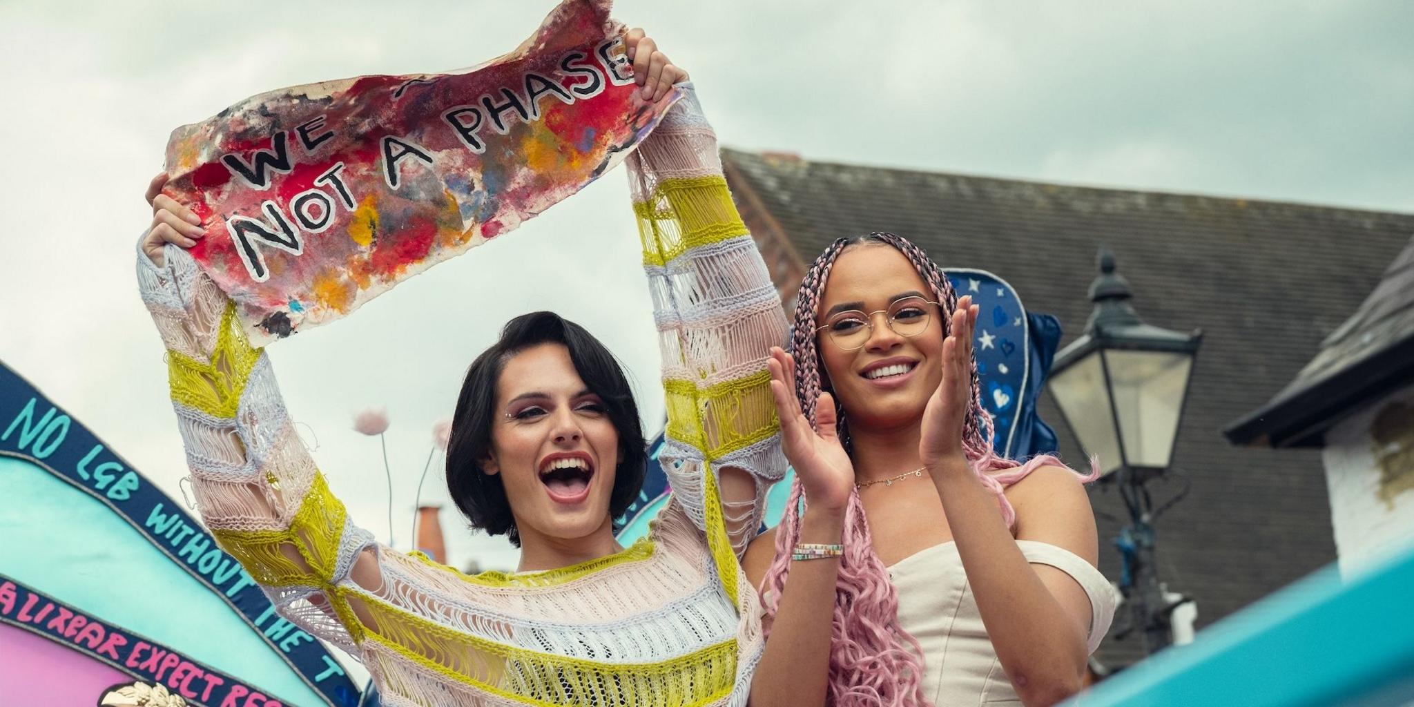 Still from Heartstopper Forever showing a Pride march with cast members Bel Priestley and Yasmin Finney.