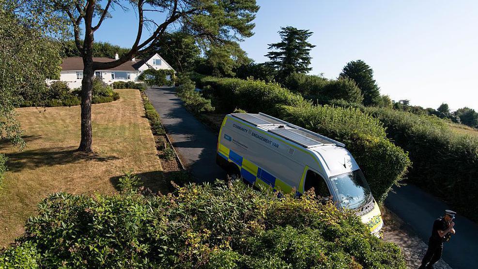 A slightly aerial view showing the home of Ann Widdecombe. A police car is parked at the beginning of the drive with a police man standing on guard