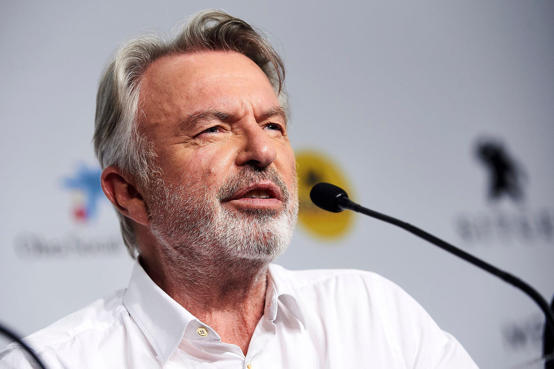 A head and shoulders crop of Neill looking away from camera while speaking into a microphone against a bokeh background, in Spain in 2019.